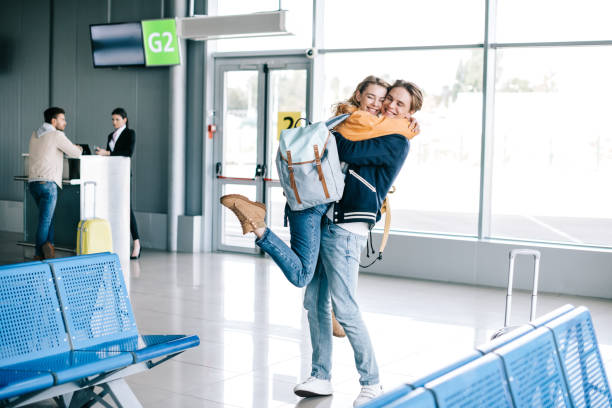 cheerful young couple hugging in airport terminal cheerful young couple hugging in airport terminal airport hug stock pictures, royalty-free photos & images