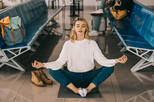 girl meditating in lotus position while waiting flight in airport terminal