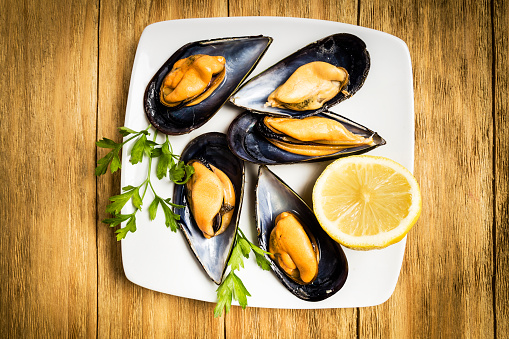 Cooked mussels with parsley and half a lemon on a white plate on a wooden table