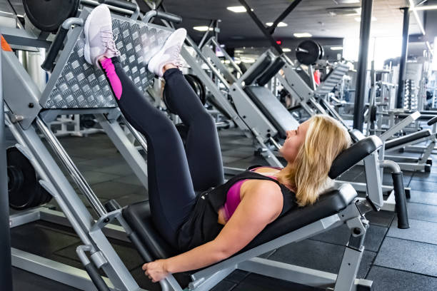 Young fit woman at the gym doing leg muscle exercise with leg press machine Female athlete at a fitness room working out with weighted leg training machine blonde female bodybuilders stock pictures, royalty-free photos & images