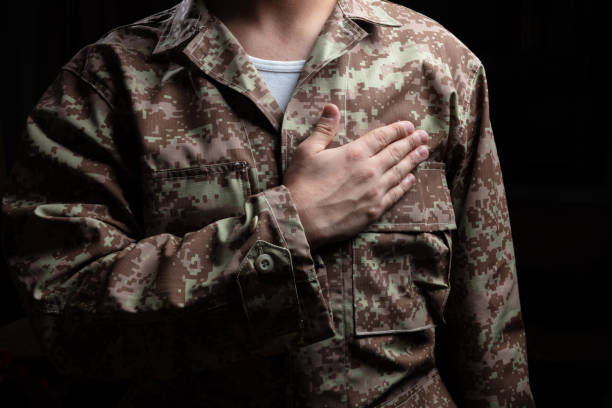 jovem soldado com a mão na posição do coração no fundo preto - armed forces war military macho - fotografias e filmes do acervo