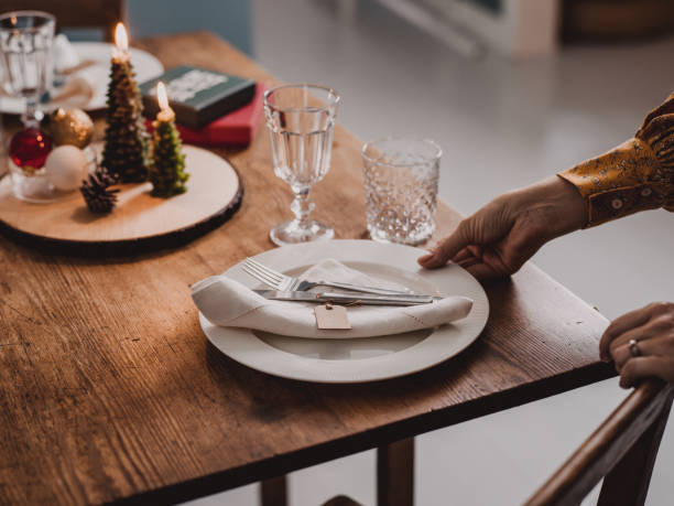 Woman setting the Christmas table preparing for dinner party Woman setting the Christmas table preparing for dinner party.
Place setting on dining table with cutlery plate napkin and decorations for Christmas. beautiful table setting stock pictures, royalty-free photos & images