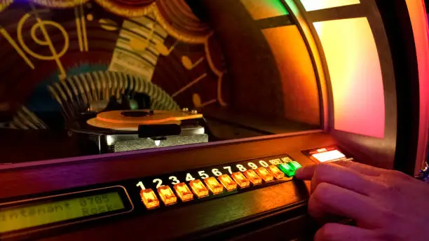 Photo of Male hand pushing buttons to play song on old musical box, selecting records
