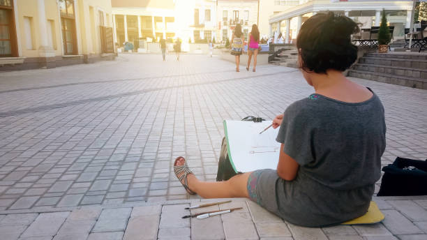 inspired female street artist sitting on pavement and painting, art and hobby - brushing human hand paintbrush artist imagens e fotografias de stock