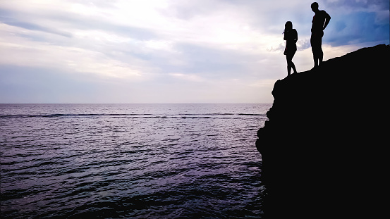 Loving couple standing on edge of rock, preparing for jump into water, romantic