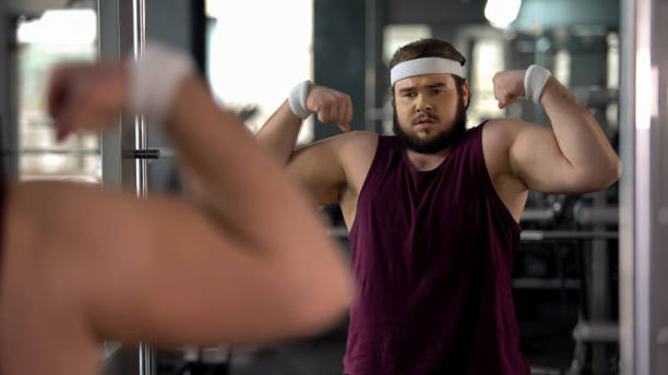 istock Positive fat man looking at mirror reflection and posing, pretending muscular 1061834084