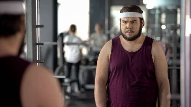 istock Fat man looking at mirror reflection in gym, mental training before workout 1061834326