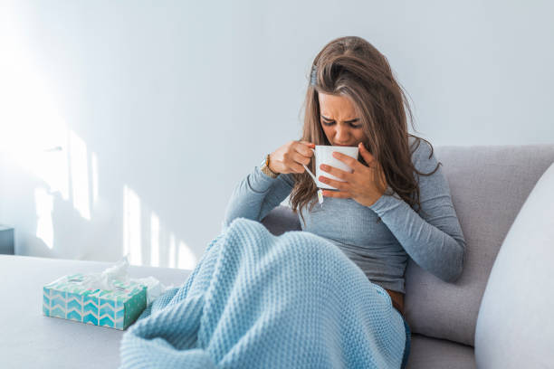 istock Young sick woman sitting on sofa drinking tea 1061848586