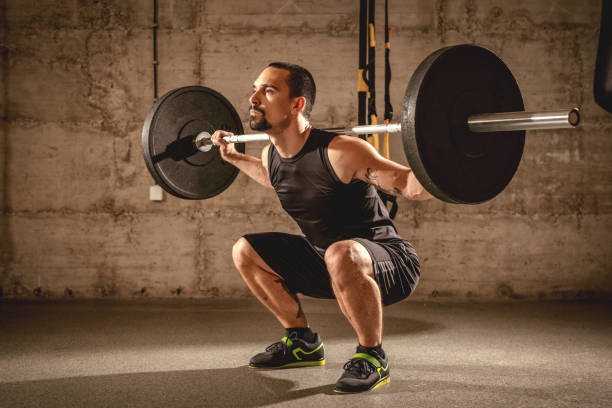 Fit And Strong Handsome young muscular man doing squat exercise with barbell at the gym. squatting position photos stock pictures, royalty-free photos & images