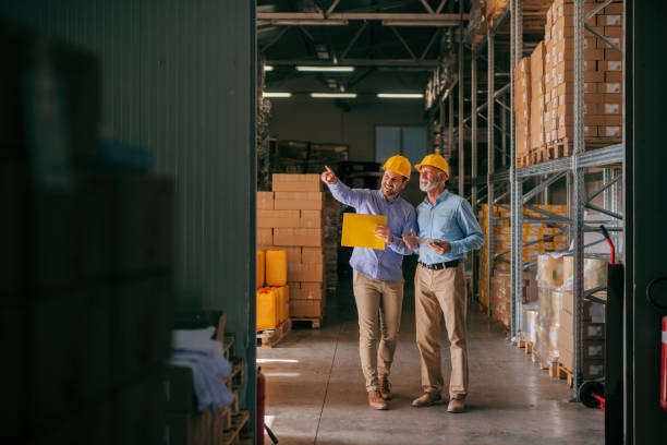 istock Colleagues walking in storage and checking documentation, on heads helmets. Younger worker pointing on boxes. 1061868466