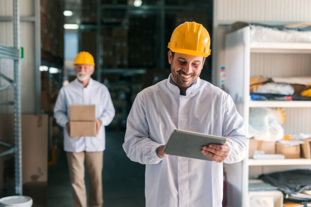 istock Young Caucasian worker using tablet while standing in warehouse. In background coworker carrying boxes. 1061868844