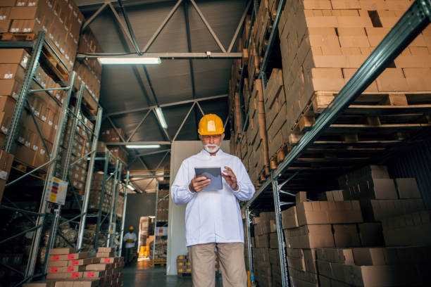 istock Senior worker using tablet and standing in storage. Protective helmet on head. 1061868872