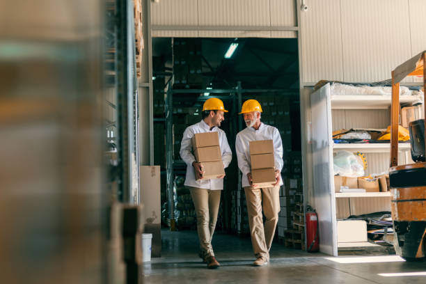 istock Coworkers carrying boxes with helmets on heads. Storage interior. 1061868910
