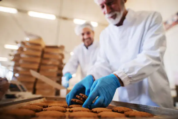 Close up of man picking cookies while other one packing in boxed. Food factory interior.