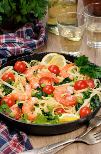 海老フライ、エンドウ豆、トマト、サイダーのガラスのテーブルの上のフライパンでほうれん草のパスタ。 - carbohydrate diabetes pasta food ストックフォトと画像