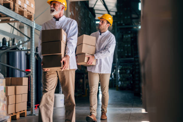istock Coworkers carrying boxes with helmets on heads. Storage interior. 1061871200