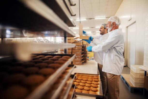 istock Workers packing cookies in boxes while standing in food factory. 1061871314