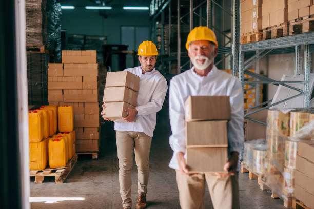 istock Coworkers carrying boxes with helmets on heads. Storage interior. 1061871370