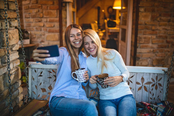 lesbian couple drinking tea and doing a selfie on a front porch - using phone garden bench imagens e fotografias de stock