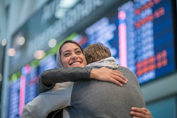 A warm embrace at the airport A young middle eastern women is greeted by her friend at the airport. She is smiling as she hugs her friend and is very happy to see him. airport hug stock pictures, royalty-free photos & images