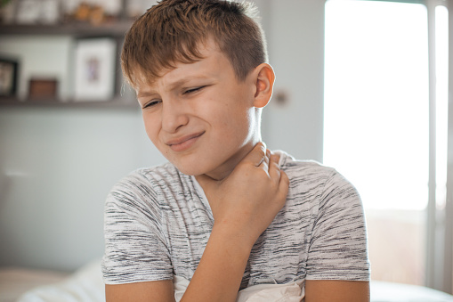 Young boy holding his neck, experiencing a sore throat