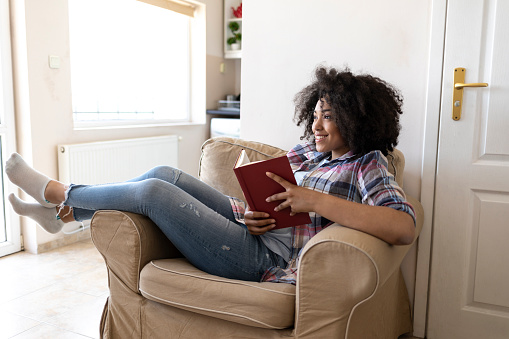 Woman reading a book at home, resting on sofa.