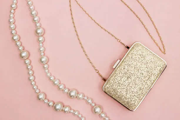 Golden purse and pearl necklace on pink background. Beauty and fashion concept.