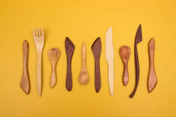 Handcrafted wooden utensils on yellow background. Fork, spoons and knives.