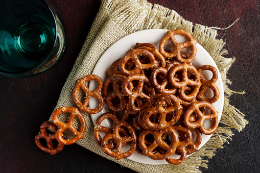 A bowl full of mini pretzels with salt on wooden background, top view, copy space.