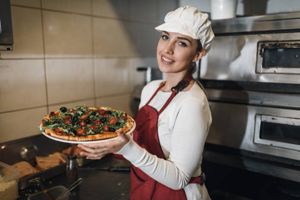 istock Young woman working in the restaurant kitchen and holding pizza 1061951962