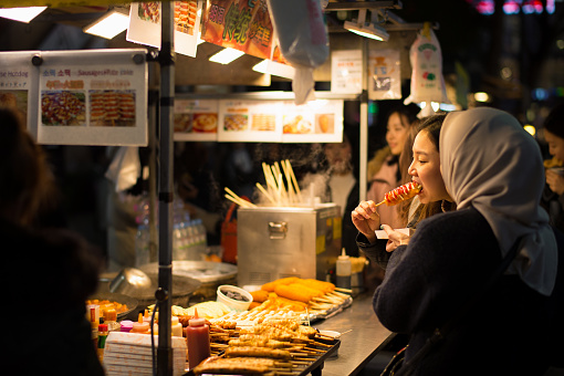 Seoul, Korea - December 20th 2017, A girl eating Korean hot dog at the booth of street food. It is the busiest street at Myeong-dong fashion district in Seoul. 서울 명동