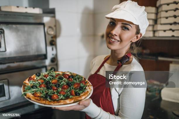 Young Woman Working In The Restaurant Kitchen And Holding Pizza Stock Photo - Download Image Now