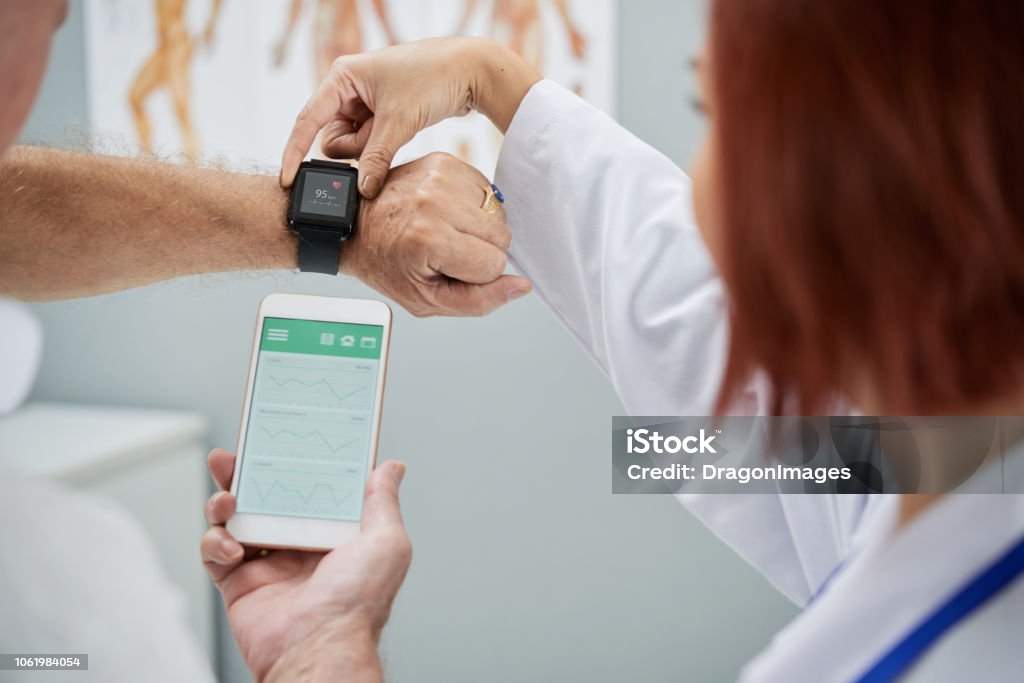 Synchronizing devices Doctor showing senior patient how to synchronize health app in smartphone and smartwatch Healthcare And Medicine Stock Photo