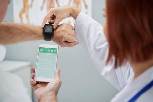 Synchronizing devices Doctor showing senior patient how to synchronize health app in smartphone and smartwatch monitoring equipment photos stock pictures, royalty-free photos & images