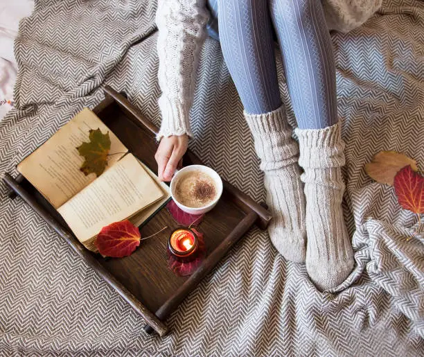 Cozy fall indoor female with woolen socks, coffee and candle, soft cozy bed blanket