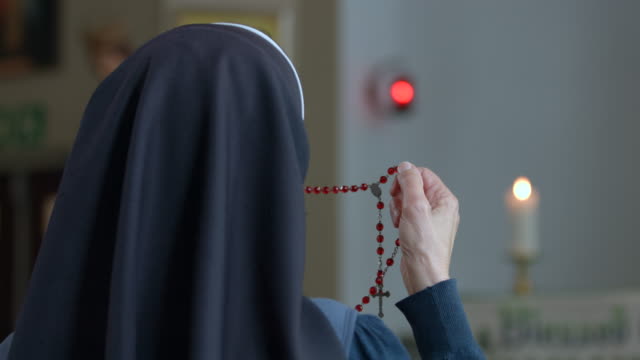 View from back of a religious sister holding rosary and praying.