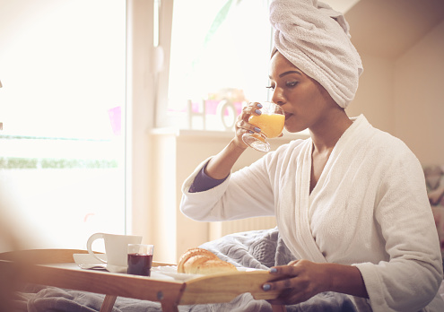 This morning started in the right direction. African American woman sitting on bed and having breakfast. Space for copy. Close up.