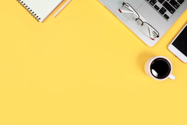istock workspace table with laptop computer, office supplies, coffee cup, cell phone and coffee cup on yellow background 1062008426