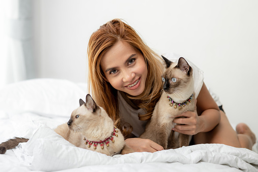 Happy Asian woman and her cats on bed.