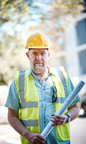 istock Mature male  building professional looks camera, serious, holding blueprints 1062033134