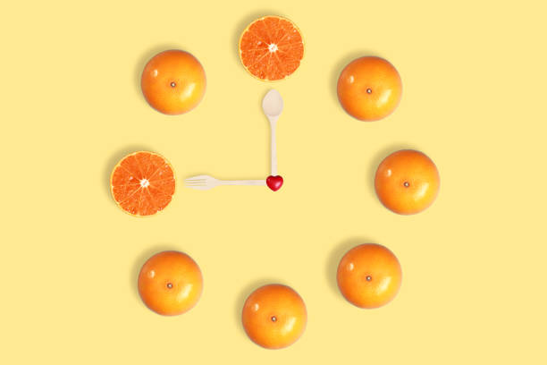 istock wall clock with orange, round slice, heart symbol, fork and spoon on yellow pastel background 1062033364