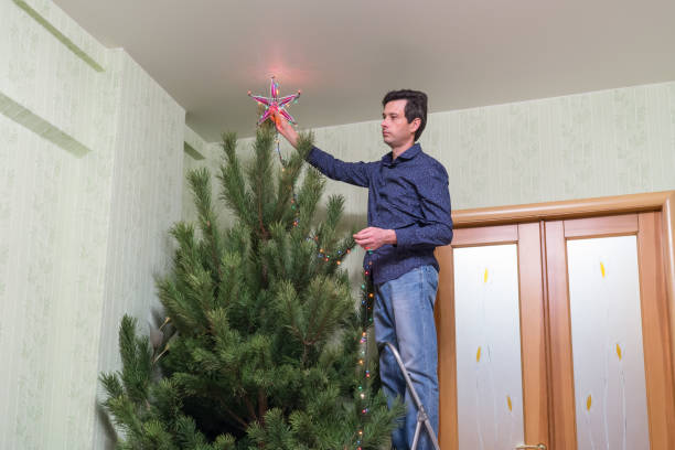 il bel uomo di mezza età decora un albero di natale con una stella - new year wall door decoration foto e immagini stock