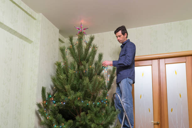 il bel uomo di mezza età decora un albero di natale con una stella - new year wall door decoration foto e immagini stock