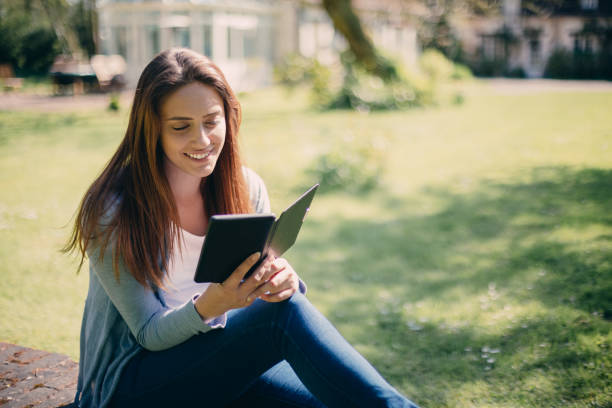 istock Beautiful girl reading e-book among nature 1062042688