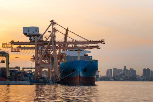 istock Container cargo ship in the export and import business and logistics international goods in urban city. Shipping cargo to the harbor by crane at sunset. 1062043738