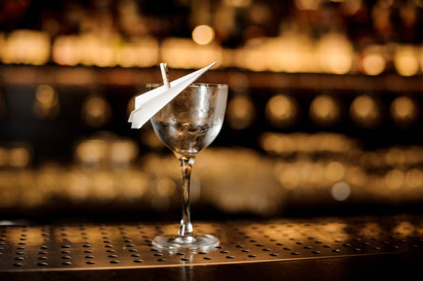istock Empty cocktail glass decorated with a paper plane on the bar counter 1062062394