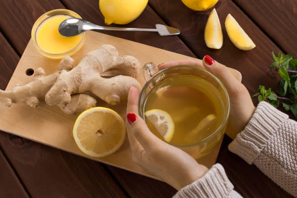 young woman in sweater holding a cup of lemon tea with ginger and honey lemon tea on wooden table ginger stock pictures, royalty-free photos & images