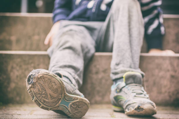 old broken shoes of a little boy as a symbol for child poverty - fome imagens e fotografias de stock