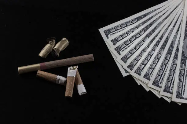 cigarette butts and american dollars on a dark background concept of financial costs for addictions and drugs