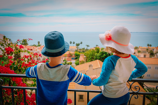 little boy and girl looking at city from balcony with sea view, family travel